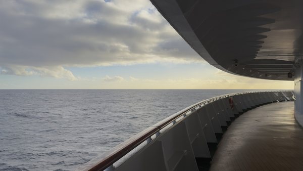 A ship deck curving toward the horizon over the sea in late afternoon light.